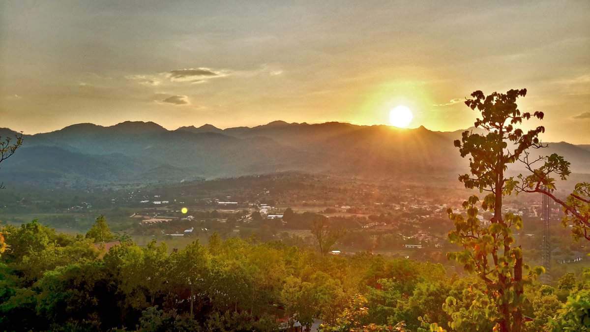 Sunset view from Wat Phra That Mae Yen, also known as the Big Buddha Temple, in Pai, Thailand, overlooking lush greenery and distant mountains.