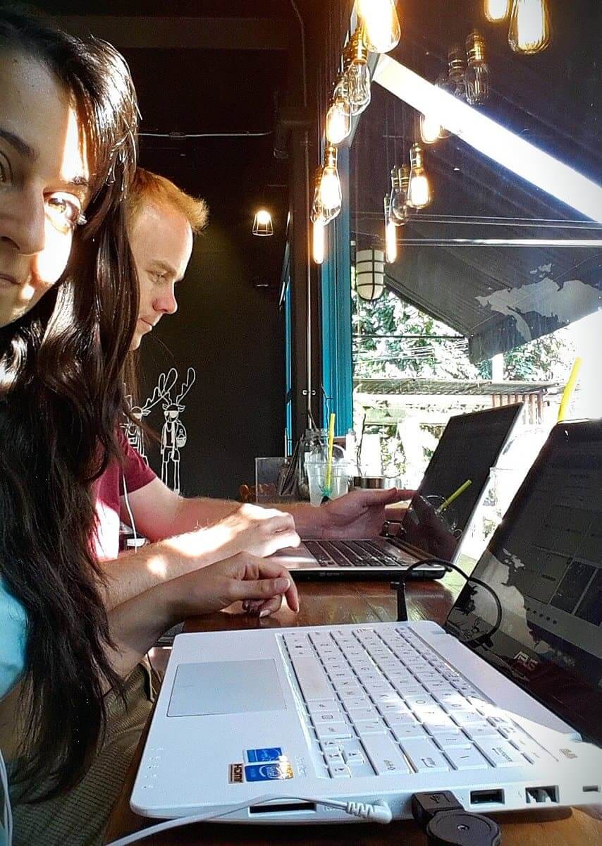 Two people working on laptops in a cozy cafe with hanging lights in Chiang Mai, Thailand.