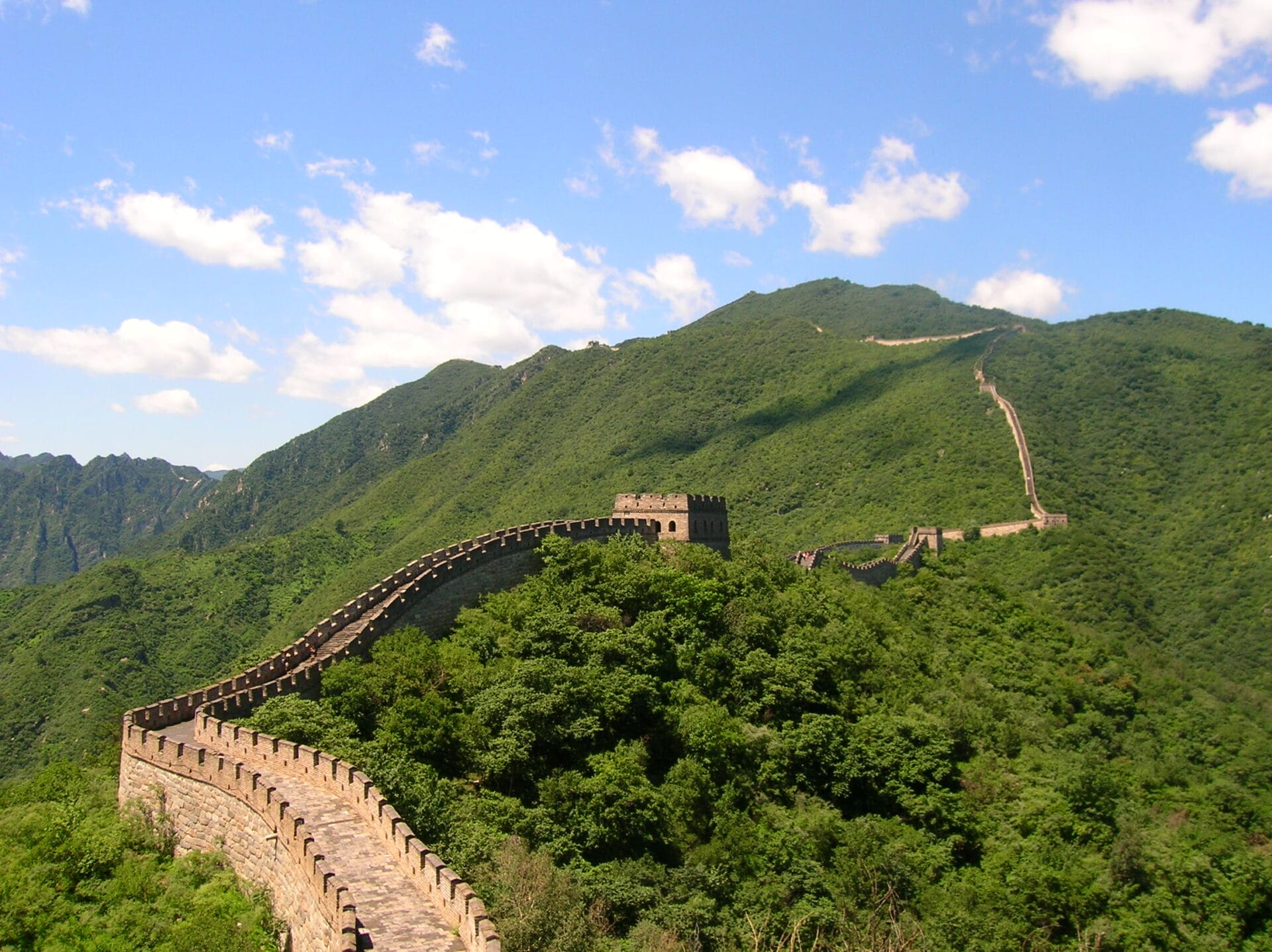 View of the Mutianyu section of the Great Wall of China with lush green mountains in the background.