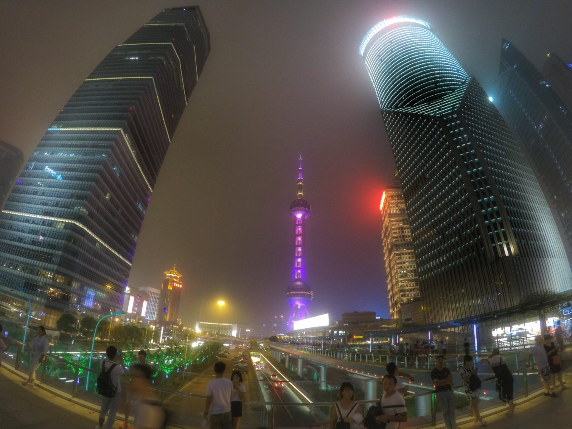 Night view of skyscrapers and the Oriental Pearl Tower in Shanghai, China, with people walking on the street.