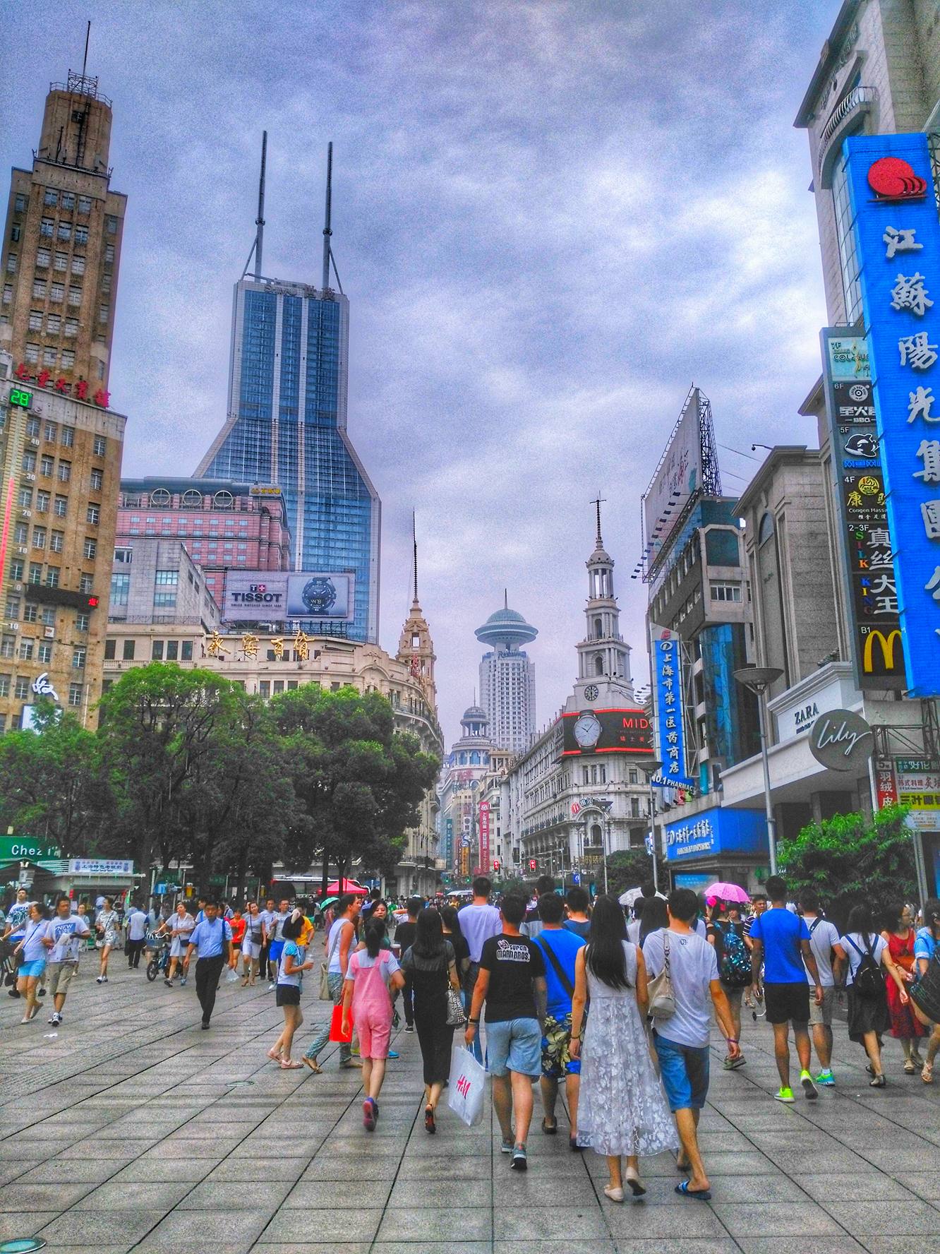 Crowded Nanjing Road with skyscrapers and vibrant storefront signs in Shanghai, China.