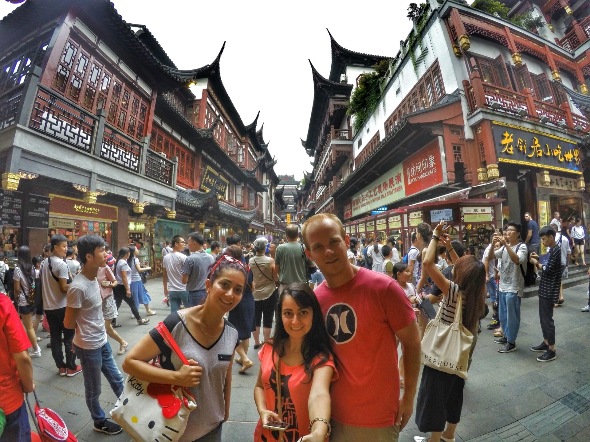 Group of people posing in front of traditional Chinese architecture at Yu Garden, Shanghai, China, with a busy marketplace in the background.