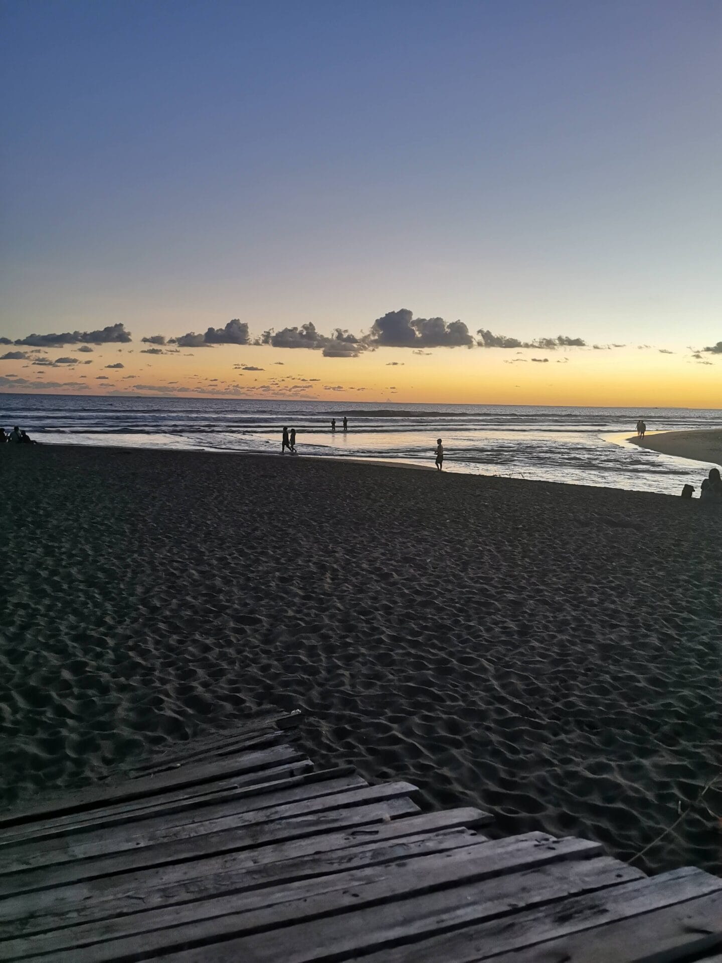 Sunset view at Kayu Putih Beach in Bali, Indonesia, with silhouettes of people walking along the shoreline and a sandy beach in the foreground.