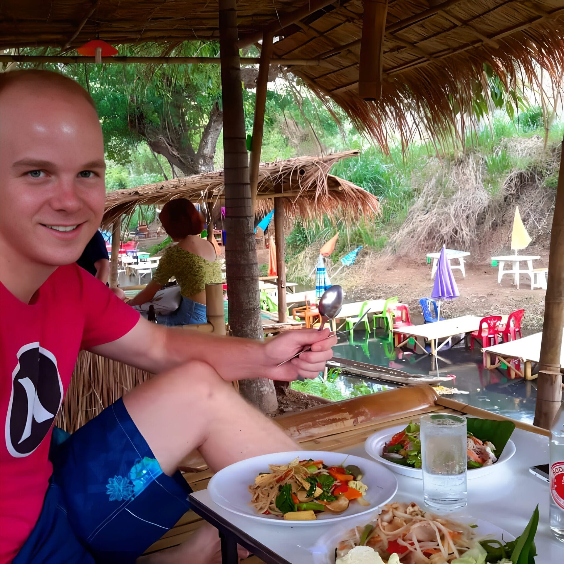 A person enjoying a meal at an outdoor restaurant with traditional bamboo huts in Chiang Mai, Thailand.