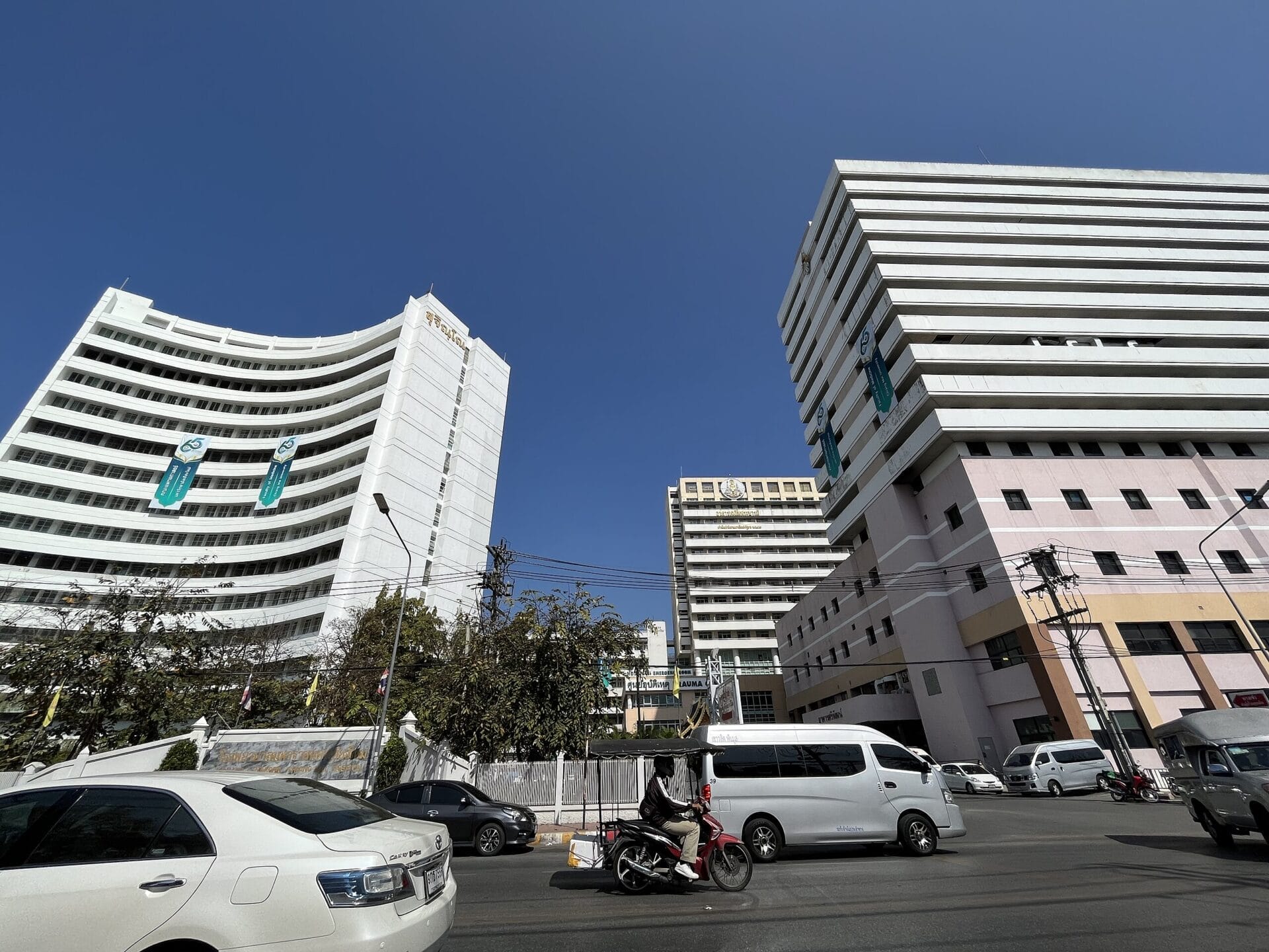 Exterior view of Maharaj Nakorn Chiang Mai Hospital in Chiang Mai, Thailand, with vehicles on the street in front.