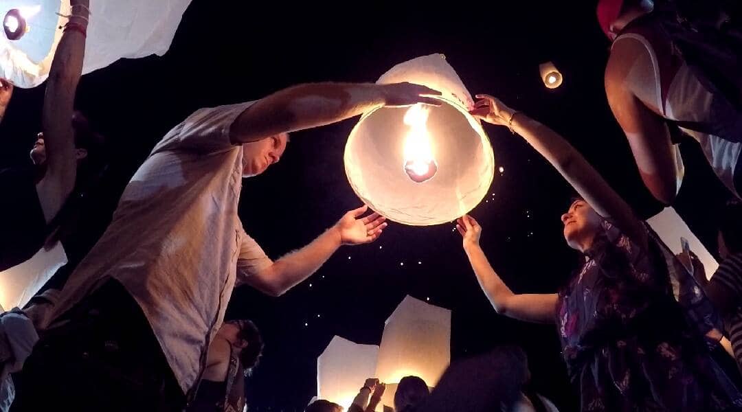 People releasing a sky lantern during a festival in Chiang Mai, Thailand at night.