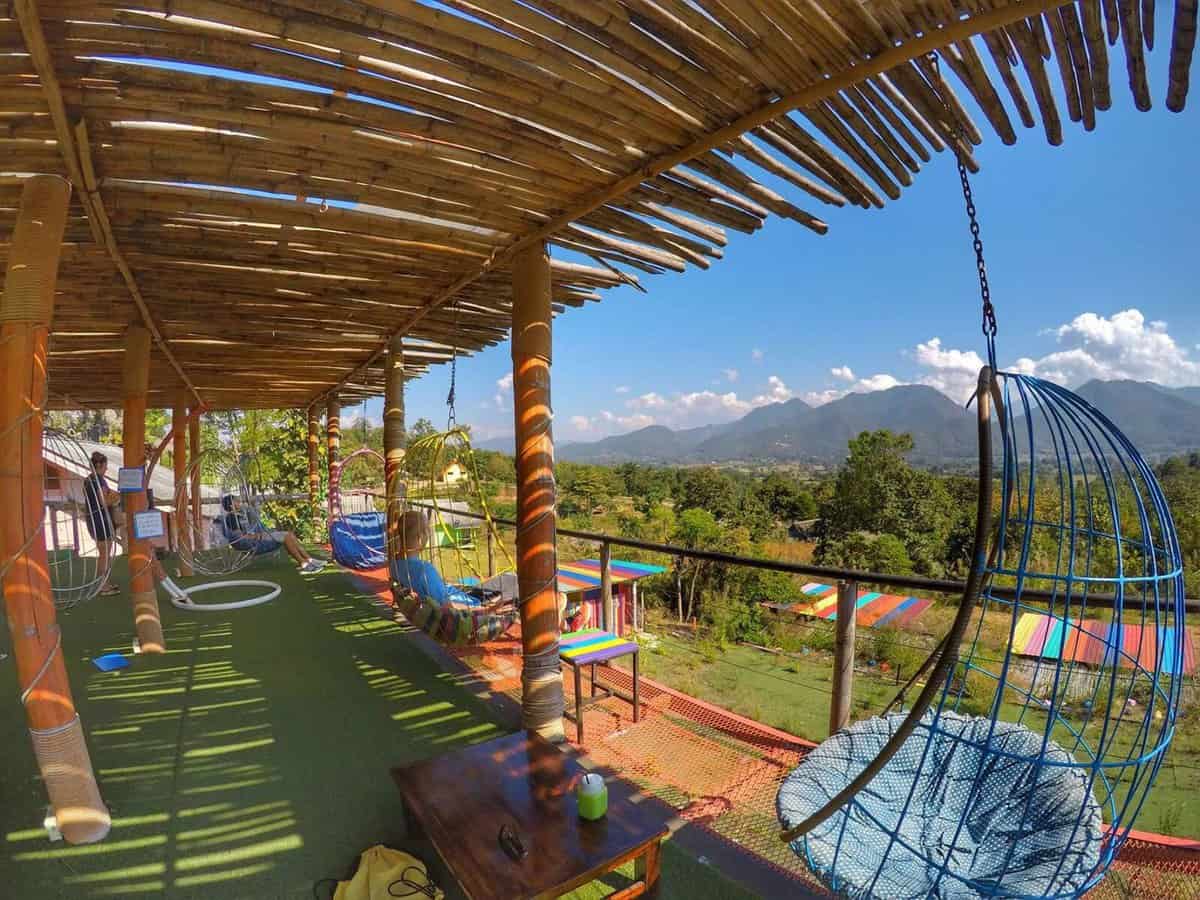 Outdoor seating area with colorful hanging chairs and scenic mountain views at Route 1094 Cafe near Pai, Thailand.