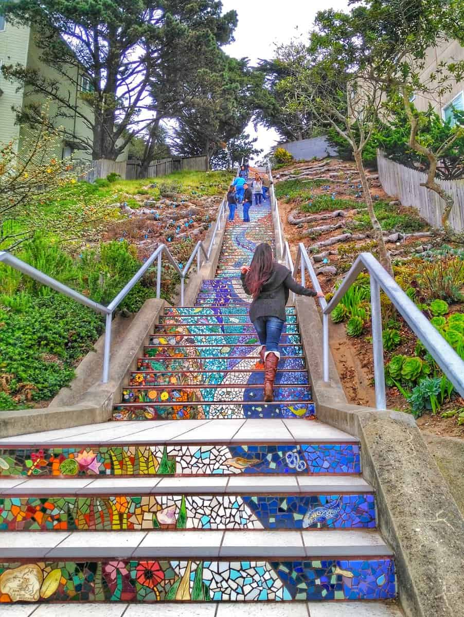 People ascending the colorful and artistic 16th Avenue Tiled Steps in San Francisco, surrounded by greenery and trees.