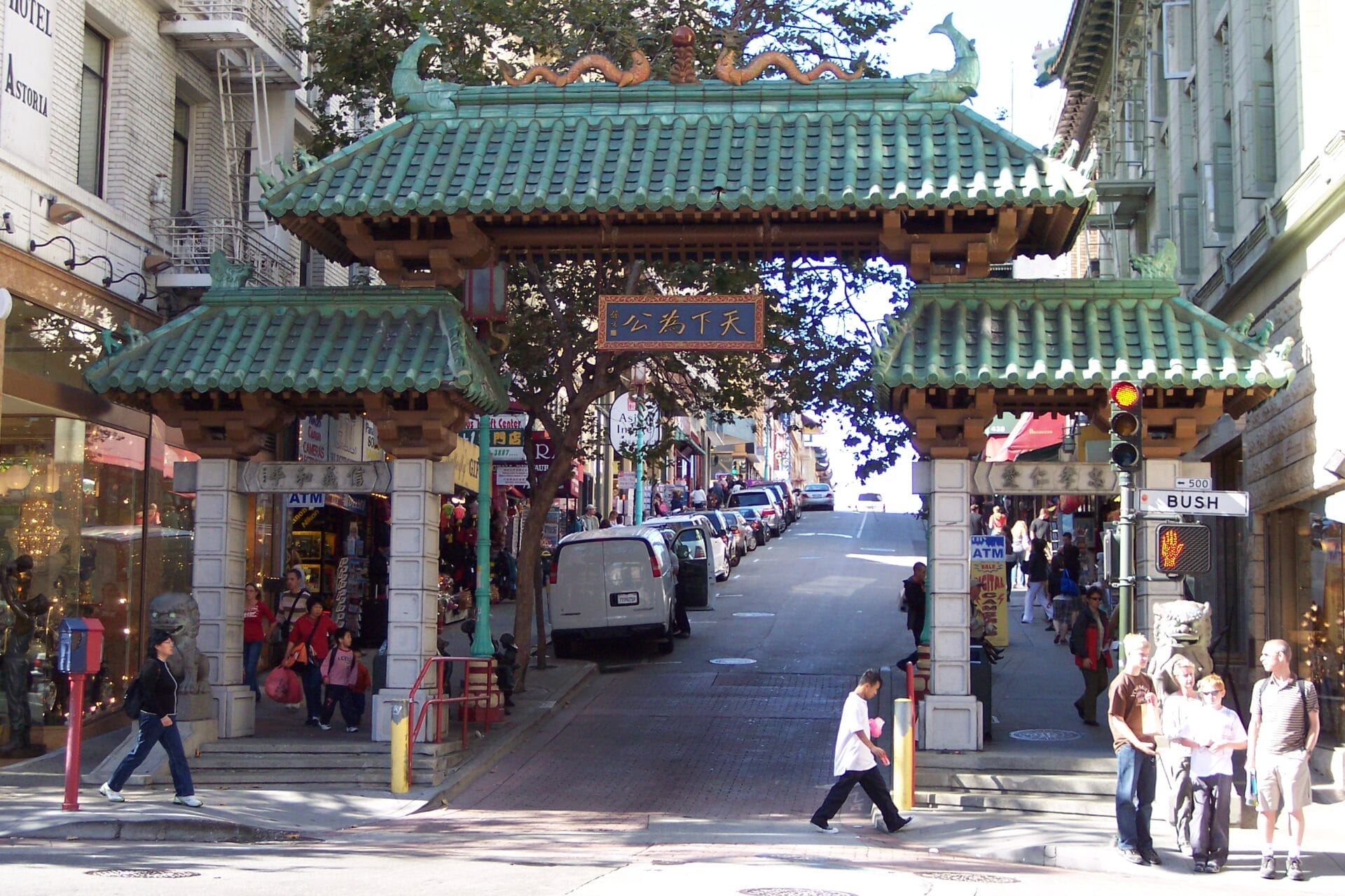 Dragon Gate entrance in San Francisco's Chinatown with pedestrians walking and cars parked along the street.