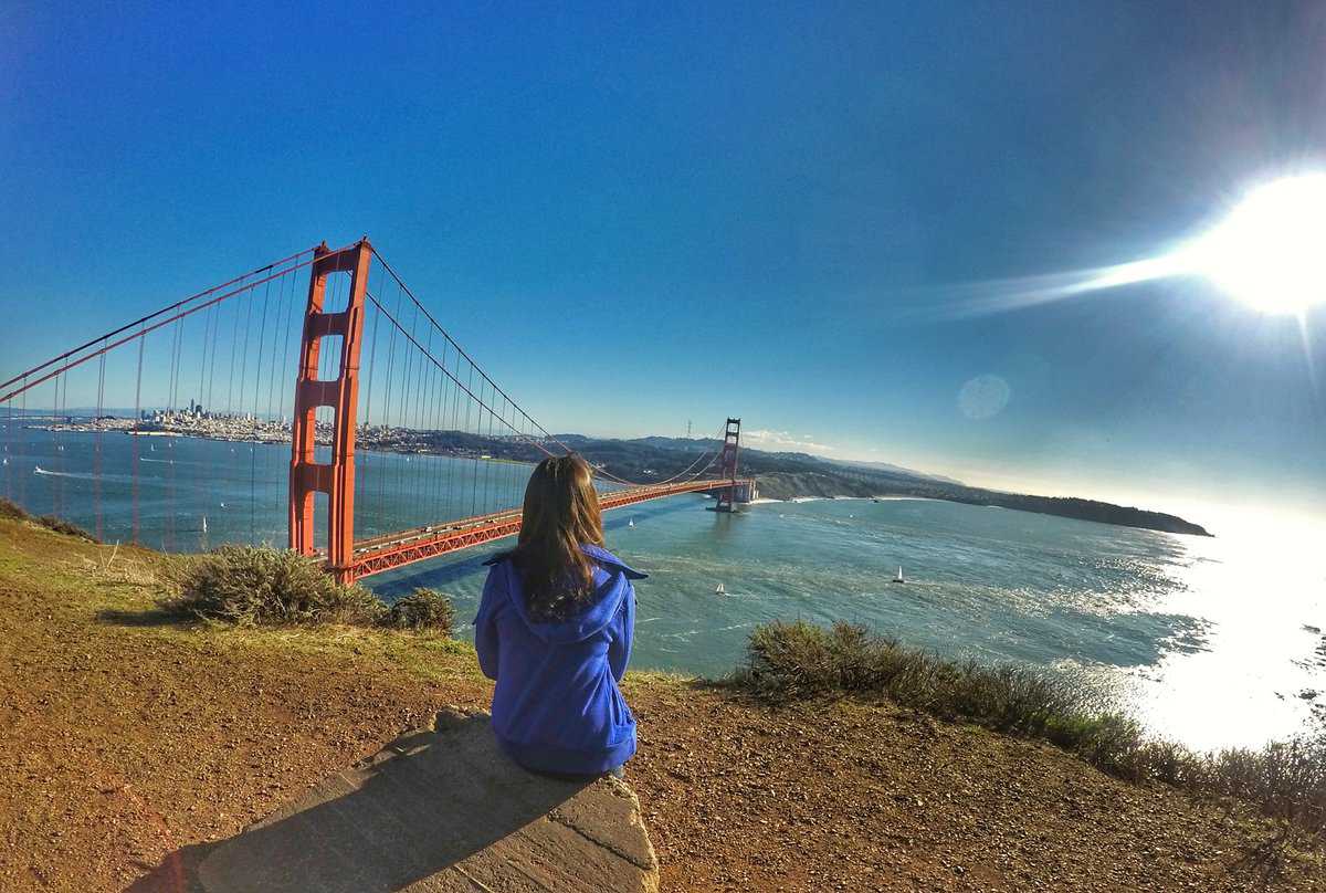 Woman sitting on ledge overlooking Golden Gate Bridge and San Francisco Bay on a sunny day.
