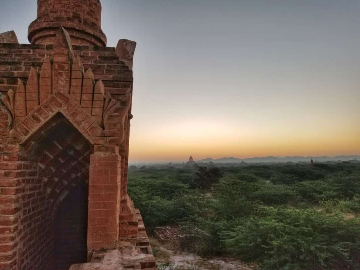 Bagan Travel - Tips Sunset view of ancient temple ruins in Bagan, Myanmar, with lush vegetation and distant pagodas.