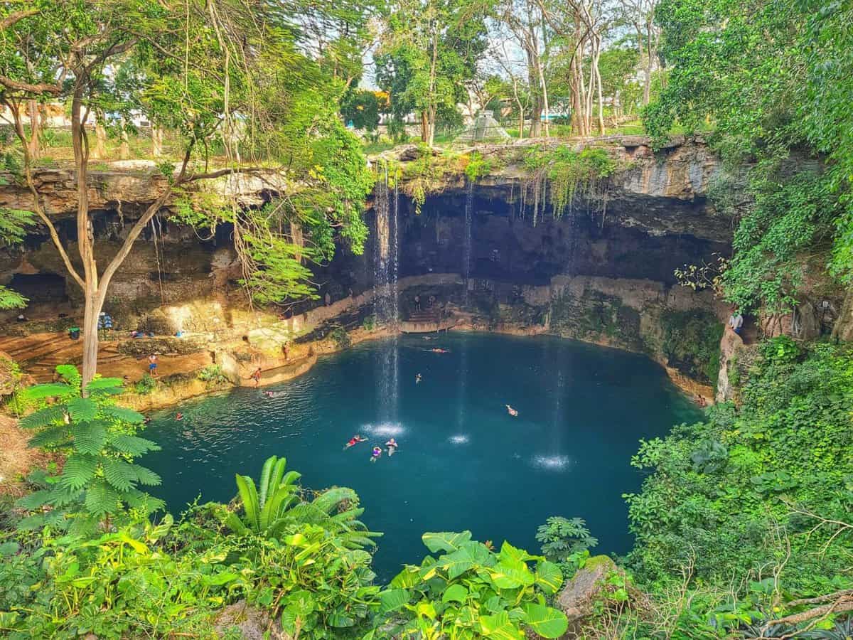 Visitors swimming and enjoying the natural beauty of the Cenote Zaci, a large sinkhole with lush greenery and cascading water in Valladolid, near Chichen Itza, Yucatan, Mexico.