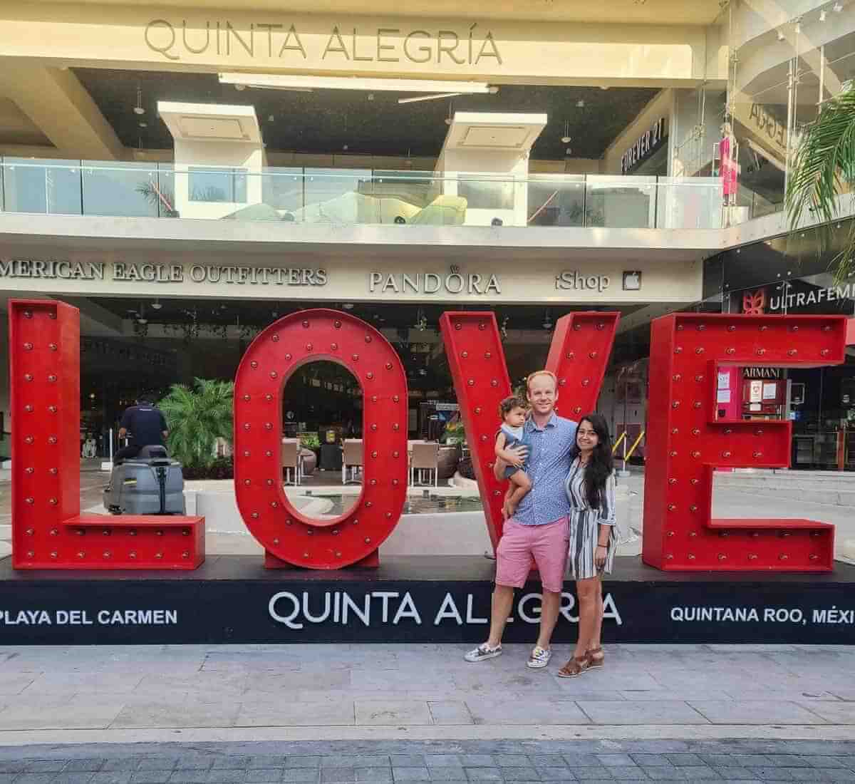 A family posing in front of a large red "LOVE" sign at Quinta Alegría shopping mall in Playa del Carmen, Riviera Maya, Quintana Roo, Mexico.