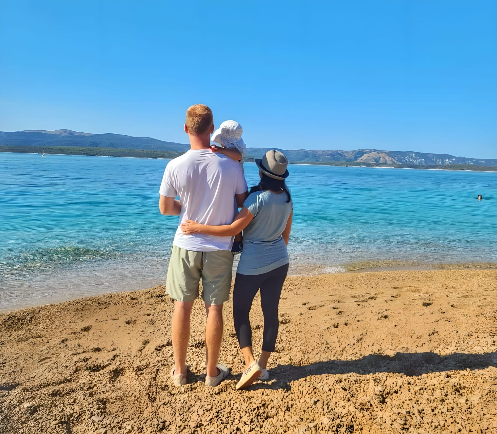 what to do with kids when visiting Croatia Family standing on a pebbled beach in Croatia, facing the clear blue waters and distant hills.