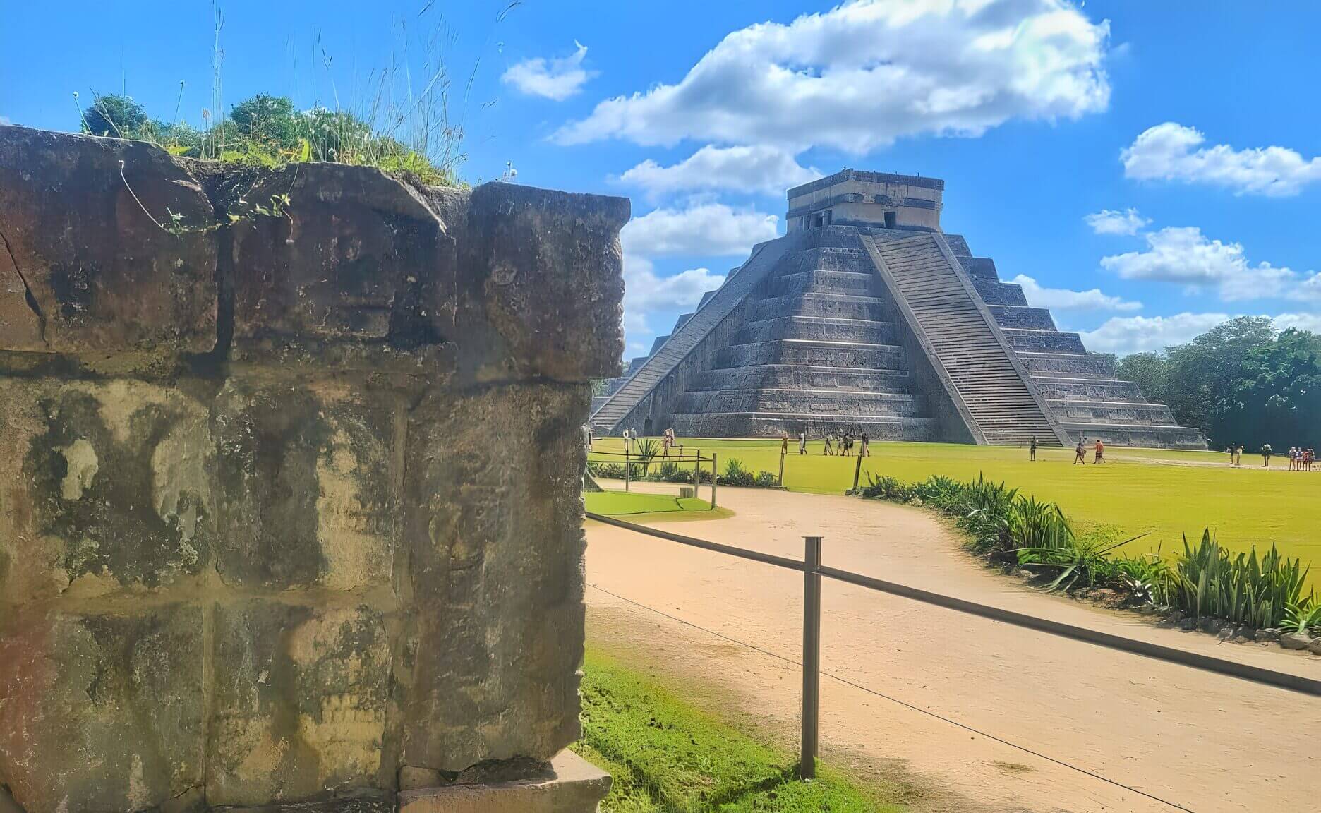 Visitors exploring the grounds near the El Castillo pyramid at Chichen Itza on a sunny day with blue skies.