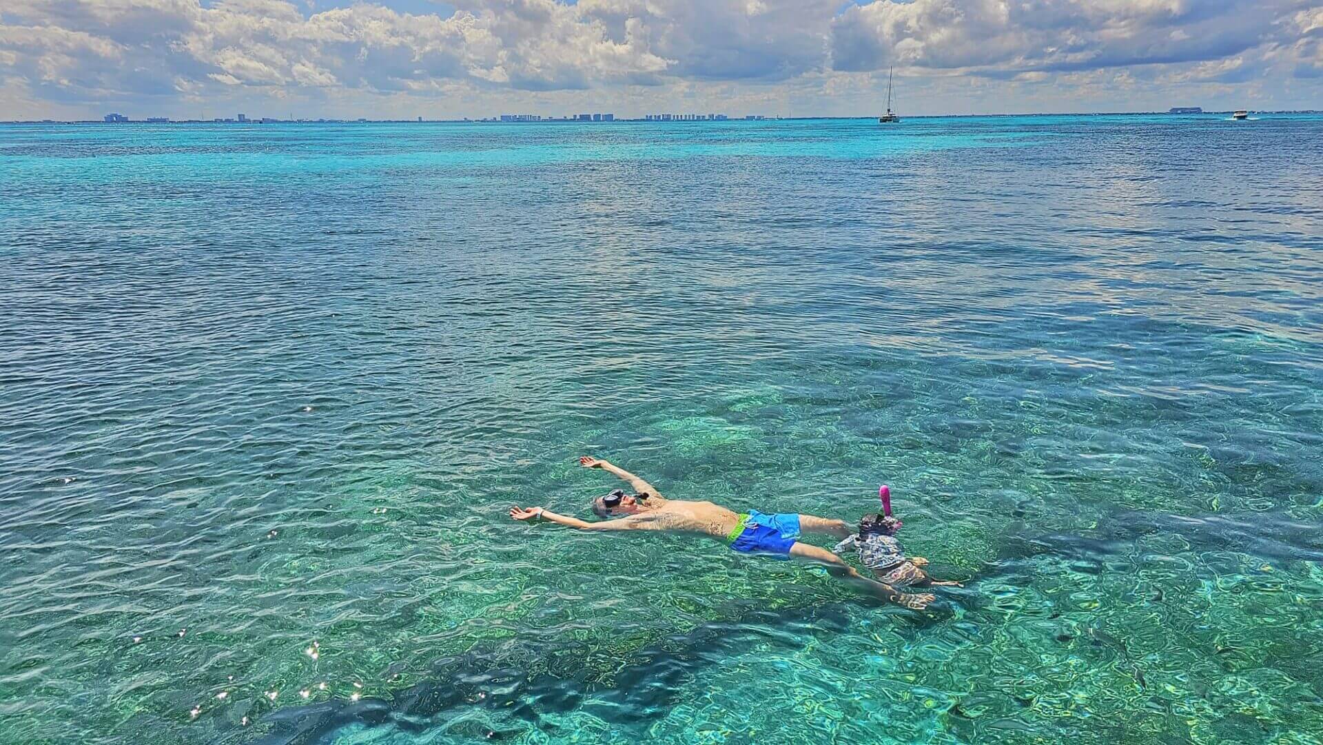 A snorkeler floating on the clear waters of Playa del Carmen, Riviera Maya, with distant views of the coastline.