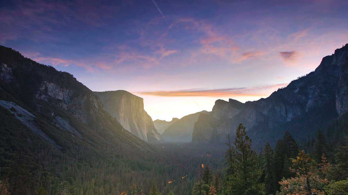 A scenic view of Tunnel View in Yosemite National Park at dawn, showcasing El Capitan and Half Dome against a colorful sky.
