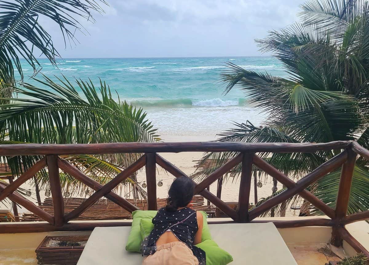 Woman relaxing on a lounge chair on a balcony overlooking the ocean at a hotel in Tulum, Mexico.