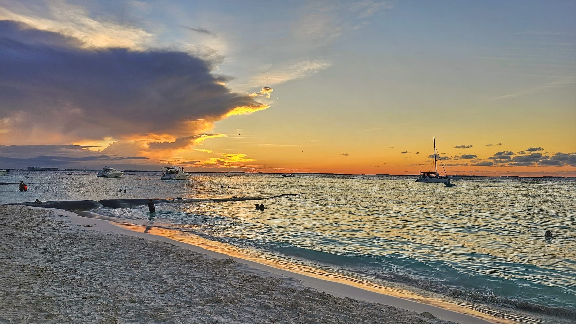 Sunset at Playa del Carmen in Riviera Maya, with boats on water and people swimming.
