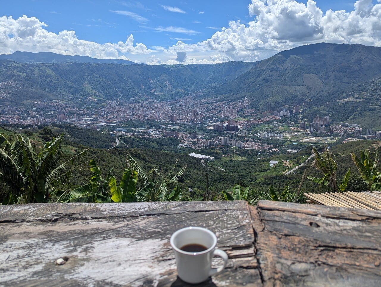 A cup of coffee on a rustic wooden table overlooking the scenic Arvi Park and cityscape of Medellin, Colombia from the Ancestral Cave coffee laboratory.