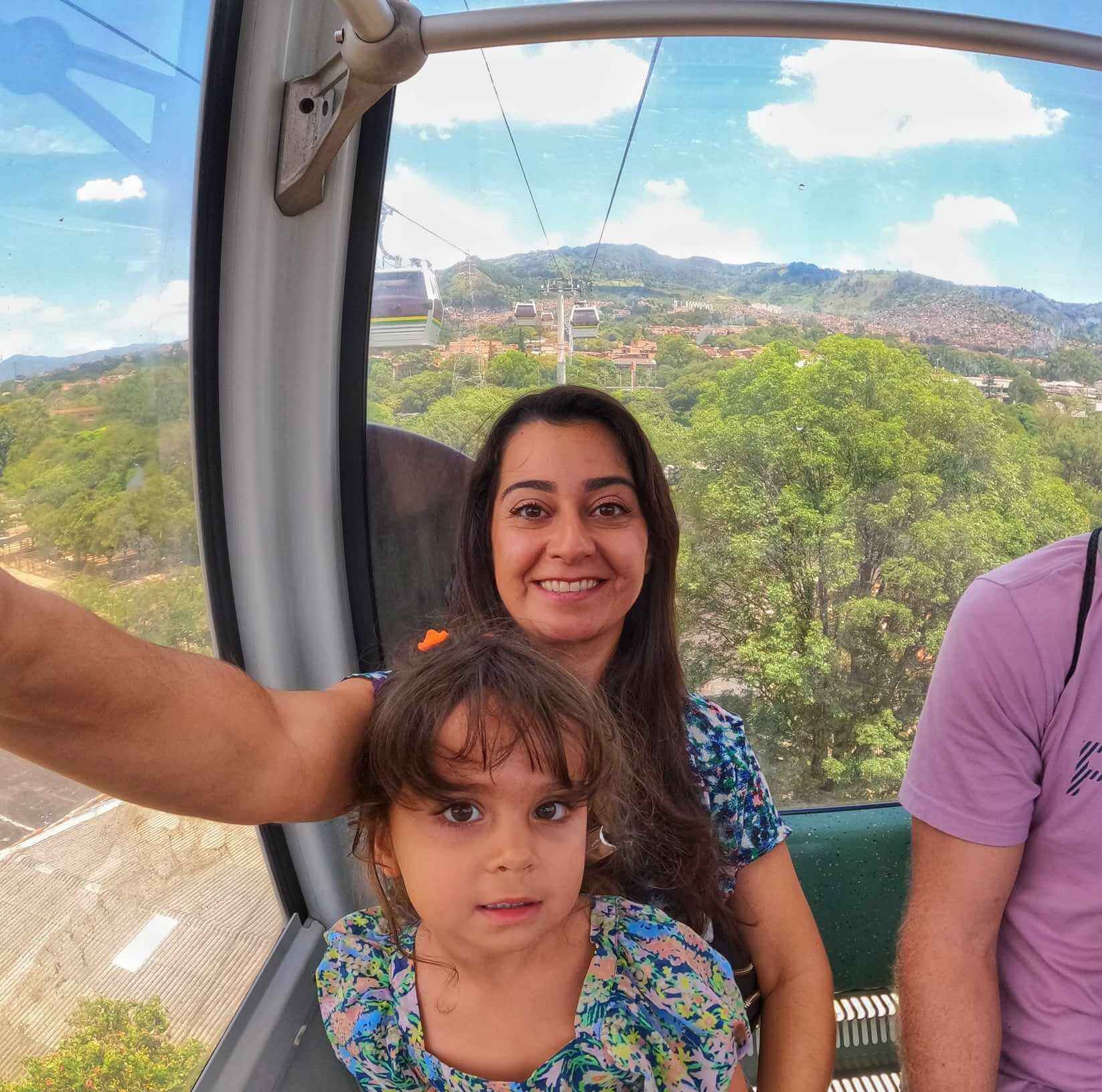 A woman and a child inside a Metrocable gondola with the scenic view of Medellin, Colombia, in the background.
