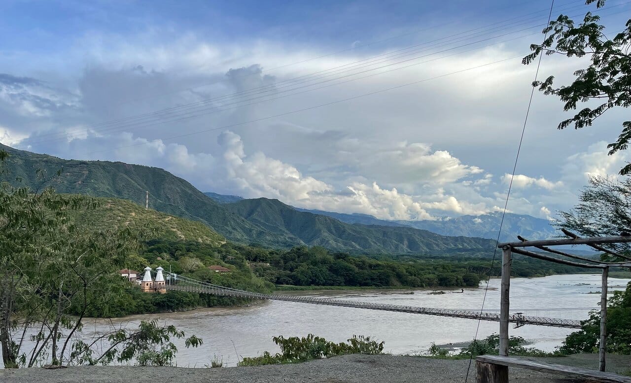Puente de Occidente spanning over a river with lush green hills and mountains in the backdrop, located in Santa Fe de Antioquia, Colombia.
