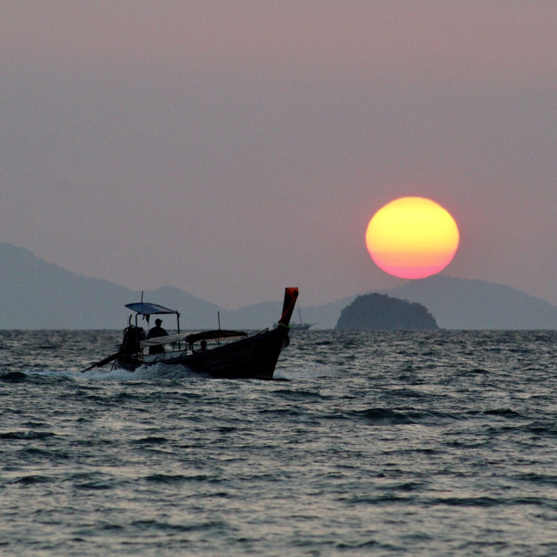 Boat sailing on the Andaman Sea with the sunset in the background, Thailand.