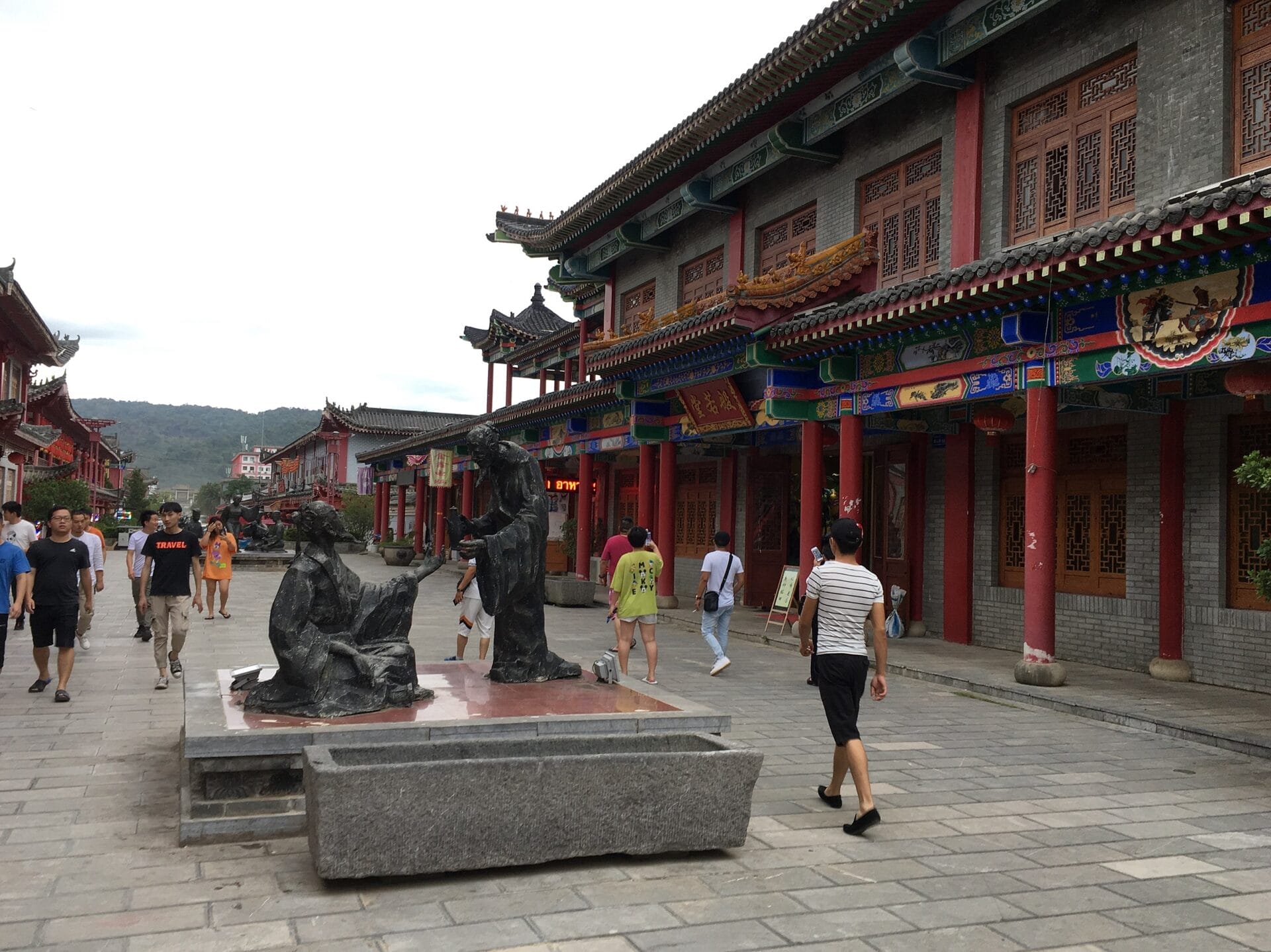 People walking along a street with traditional Chinese architecture in Chinatown, Golden Triangle Special Economic Zone, Laos. The street is adorned with colorful decorations and features a statue of two figures.