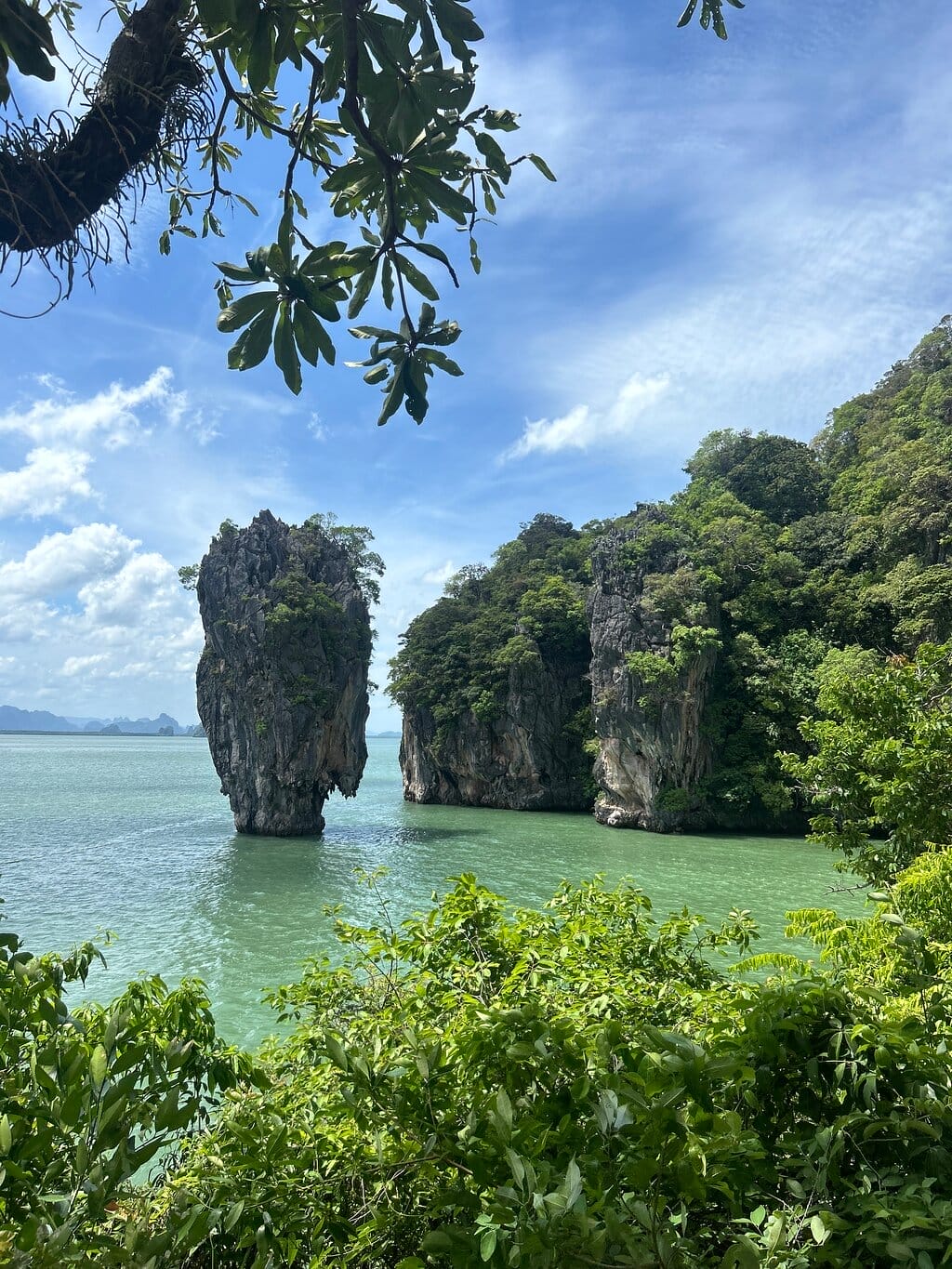 Scenic view of James Bond Island (Koh Tapu) in Thailand, featuring a towering rock formation surrounded by turquoise waters and lush greenery under a clear blue sky.