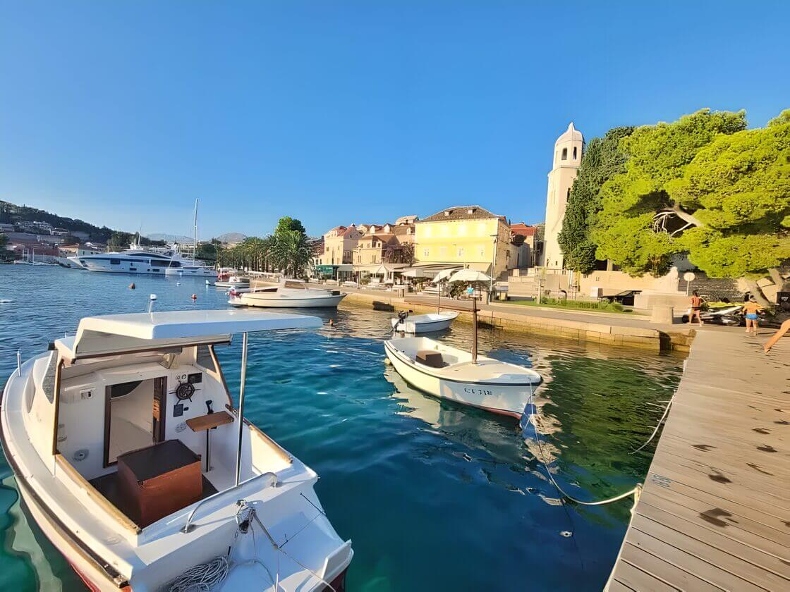 Best Family Destination in Croatia-Cavtat Boats docked along the waterfront in Cavtat, Croatia, with a view of the town's buildings and a church tower under a clear blue sky.