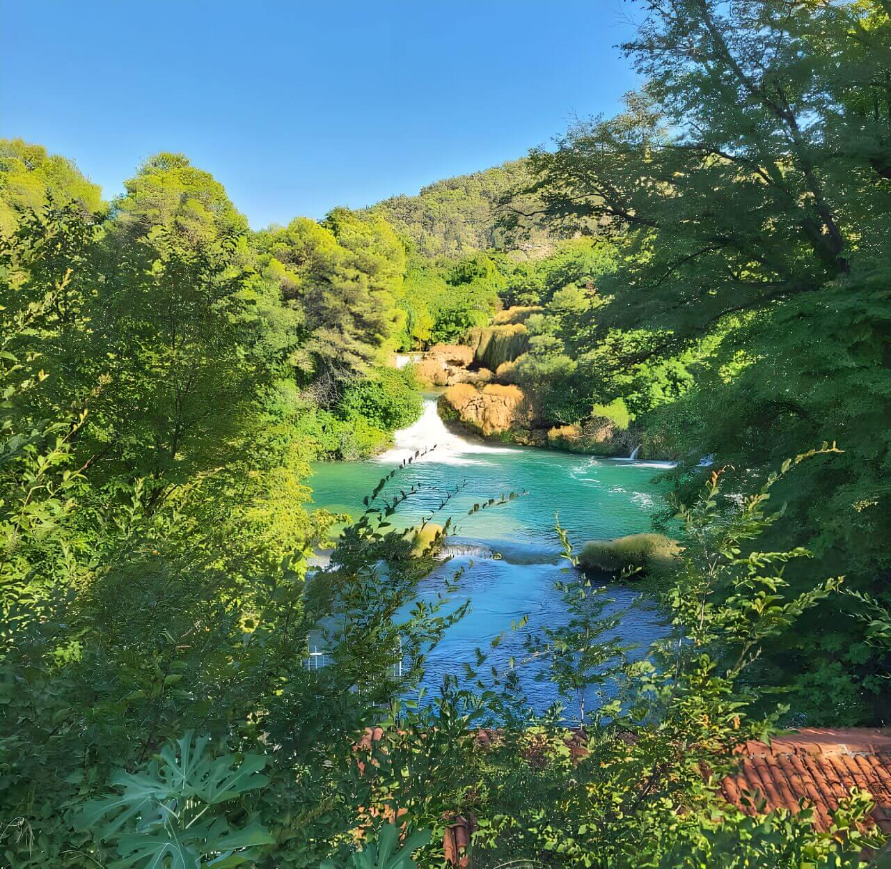 Krka Falls Croatia A scenic view of Krka National Park in Croatia showcasing a waterfall surrounded by lush greenery and a bright blue sky overhead.