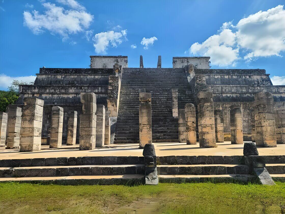 Ancient stone columns of the Temple of a Thousand Warriors at Chichen Itza under a blue sky with scattered clouds.