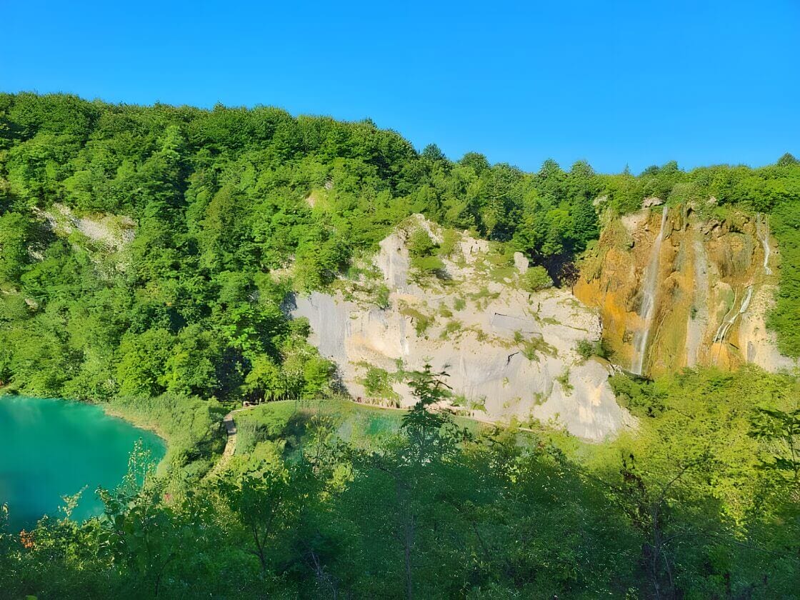 Plitvice National Park Croatia A stunning landscape of Plitvice Lakes National Park in Croatia, featuring a lush green forest, rocky cliffs, and cascading waterfalls with a clear blue sky in the background.