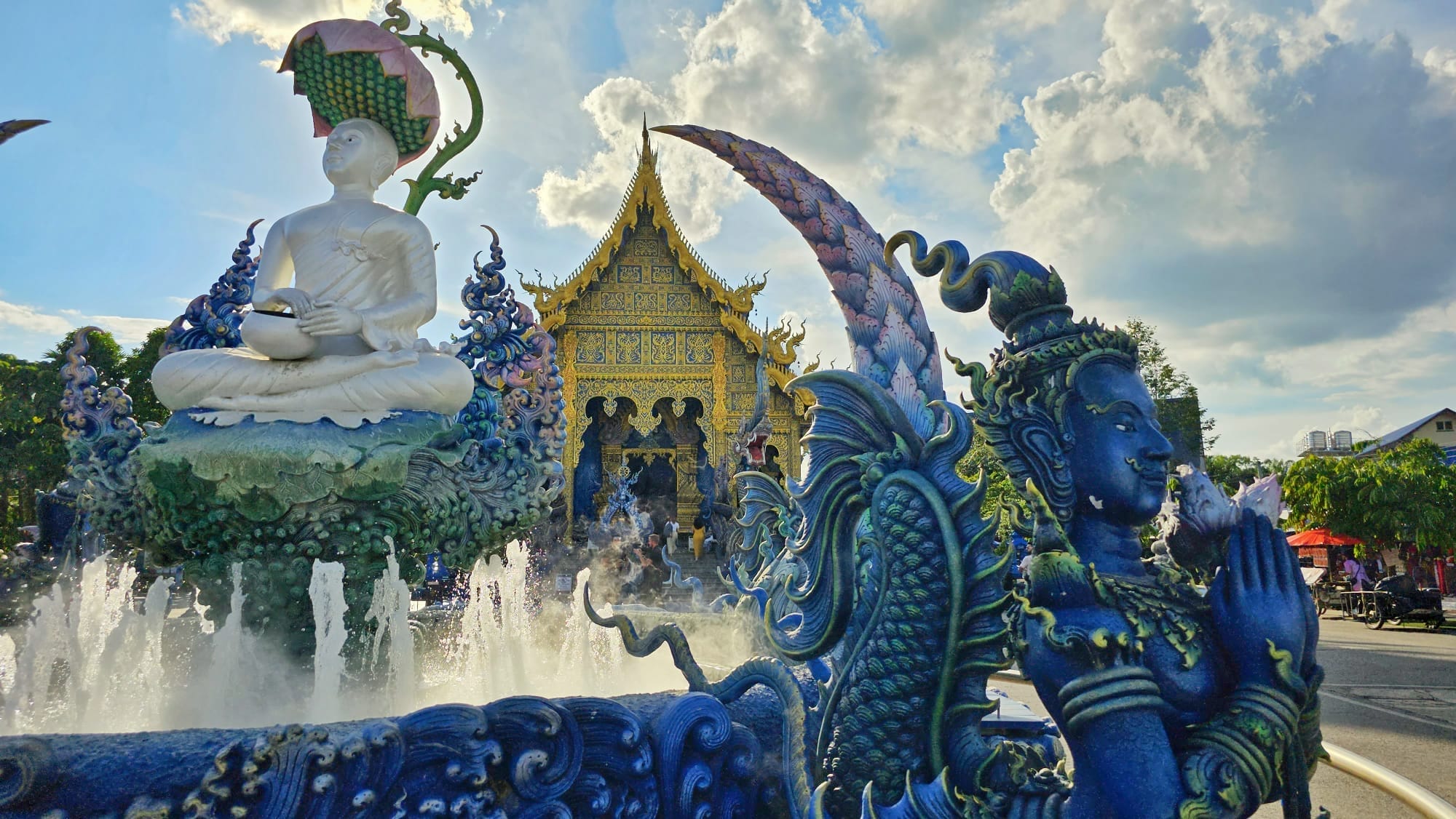 Intricately designed statues and vibrant blue sculptures in front of the main hall of Wat Rong Suea Ten, also known as the Blue Temple, in Chiang Rai, Thailand.