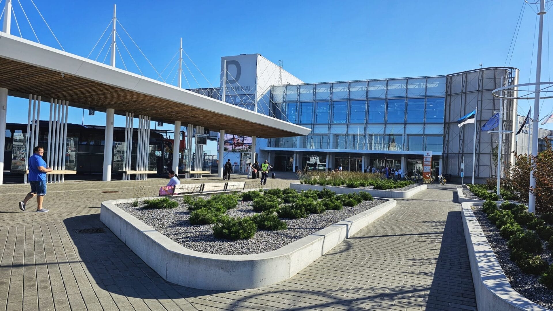 Modern ferry terminal building and outdoor area in Tallinn, Estonia with people walking and buses parked under a covered area.