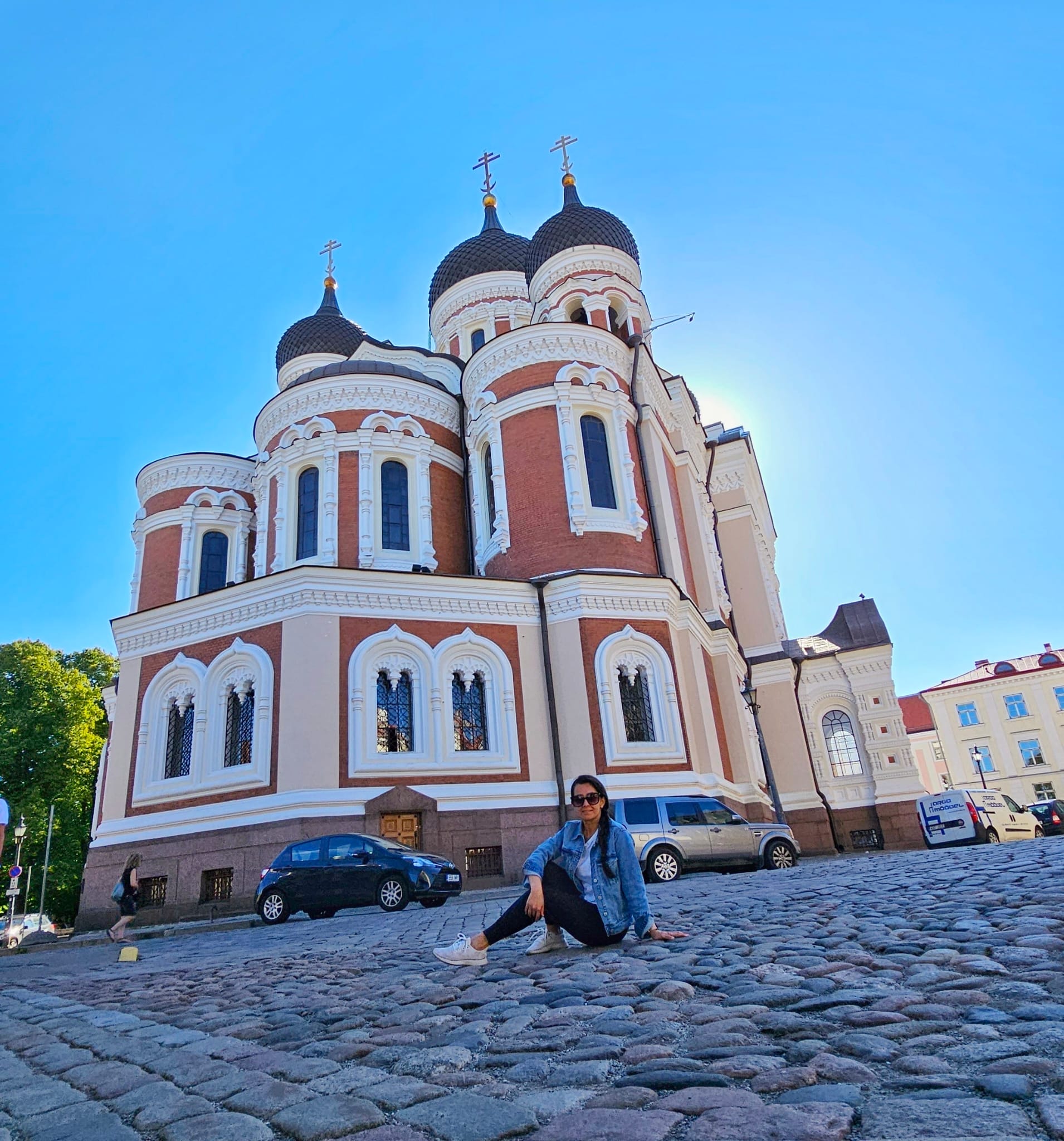 A person sitting on a cobblestone street in front of Alexander Nevsky Cathedral in Tallinn, Estonia, on a clear, sunny day.