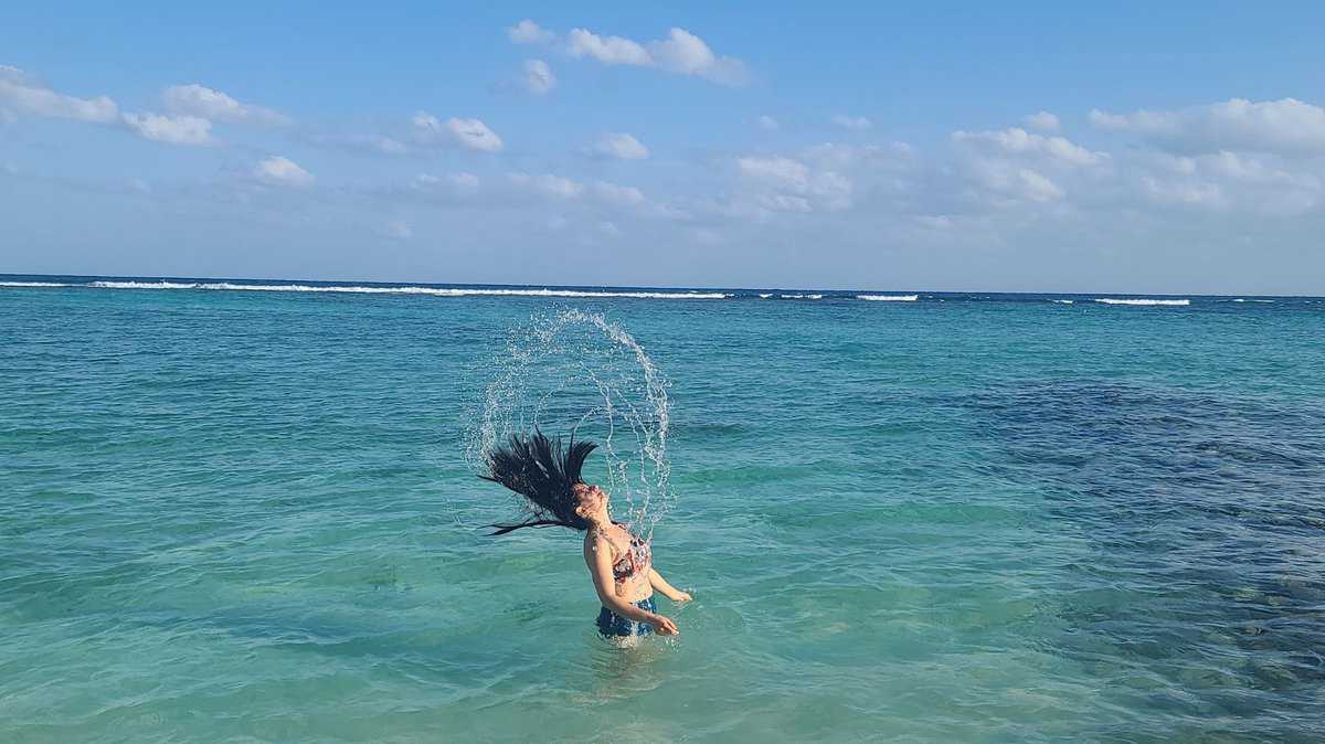 Person flipping their hair in the air while standing in the turquoise waters of Akumal, Quintana Roo, Mexico.