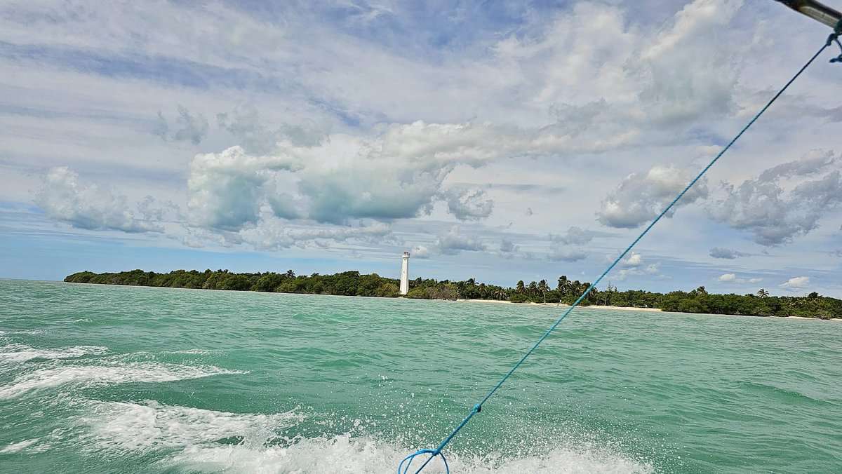 View from a boat of the turquoise waters with a distant lighthouse on the shore of Sian Ka'an Biosphere in Quintana Roo, Mexico, under a partly cloudy sky.