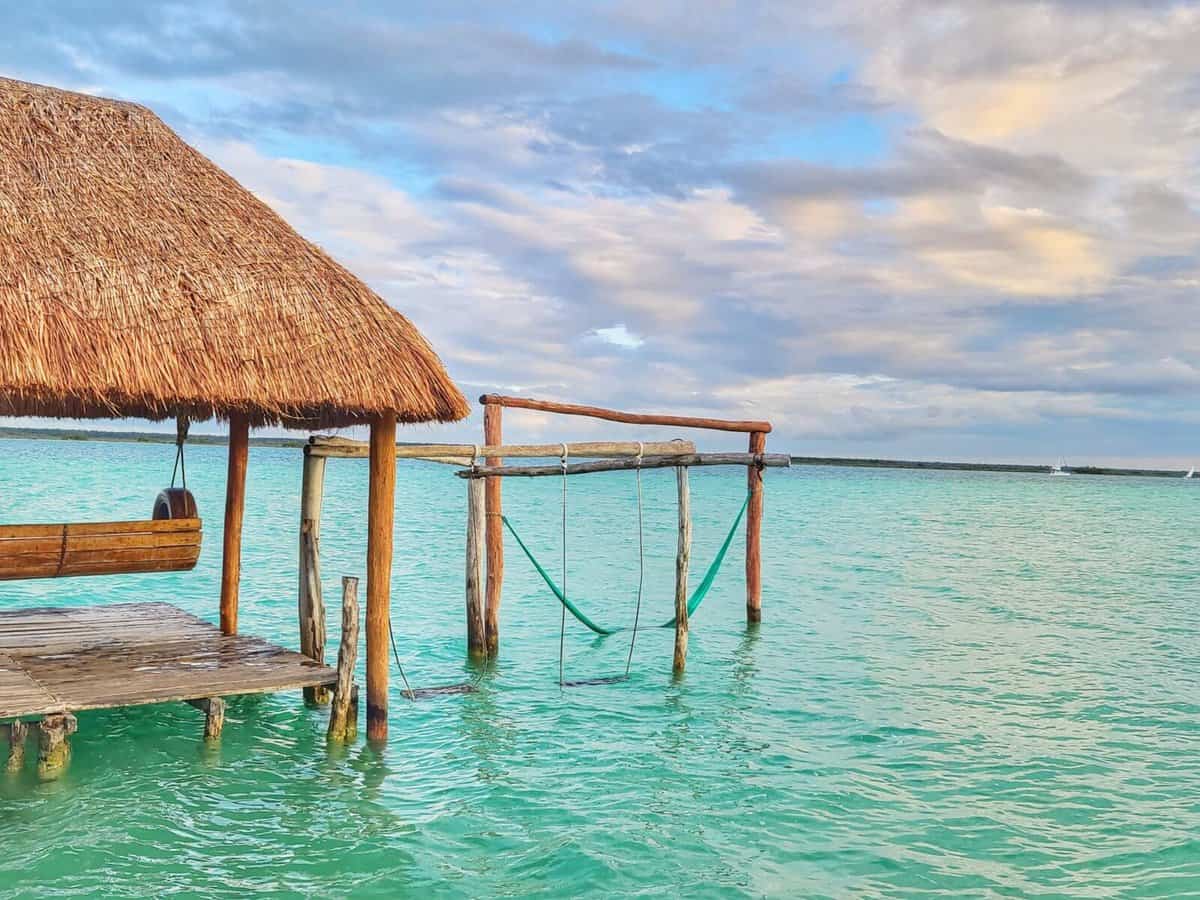 Bacalar Laguna Restaurant A wooden dock with a thatched roof and a swing over the clear turquoise waters of Bacalar Lagoon in Quintana Roo, Mexico.