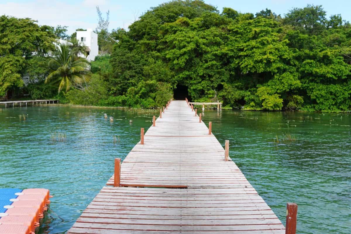 where to stay in Bacalar, Mexico Wooden pier extending over turquoise waters toward lush greenery in Bacalar, Quintana Roo, Mexico.