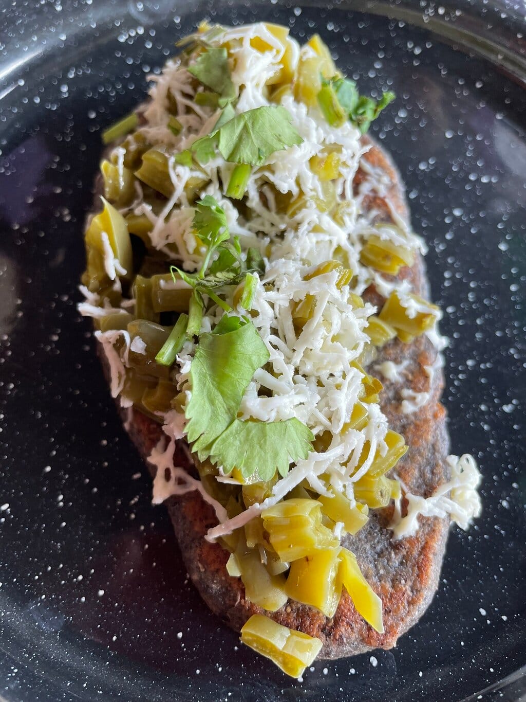 A close-up view of a blue corn sope topped with cheese and cactus, served on a dark, speckled plate in Puerto Morelos, Mexico.