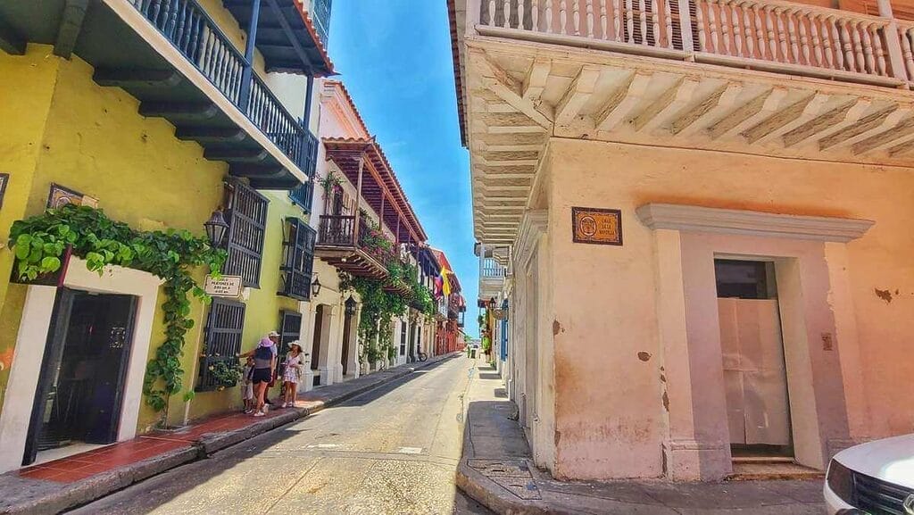 A vibrant street in the walled city of Cartagena, Colombia, featuring colorful colonial buildings and balconies adorned with lush greenery.