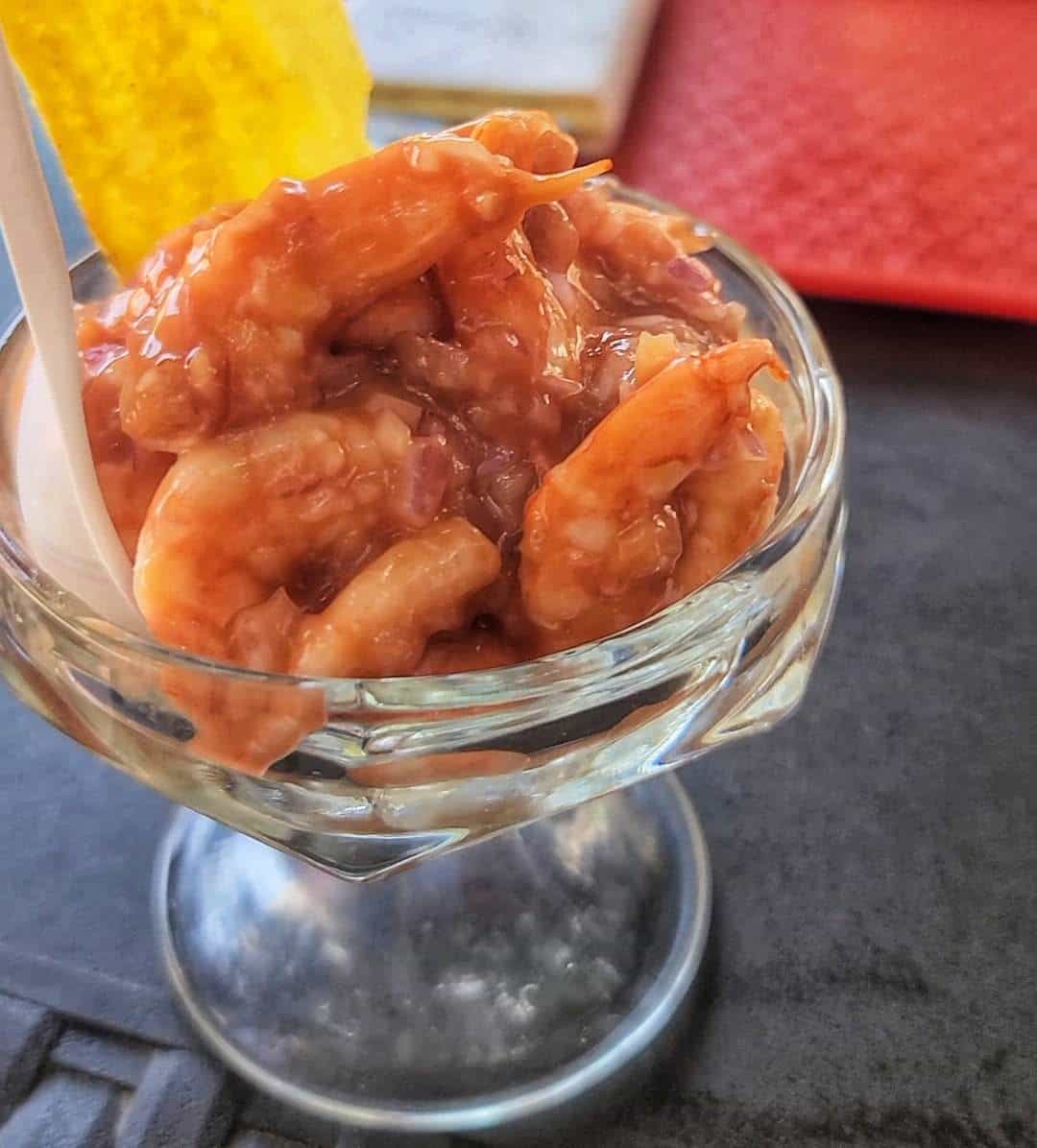 Glass dish of shrimp cocktail with a yellow plantain chip, served in Cartagena, Colombia.