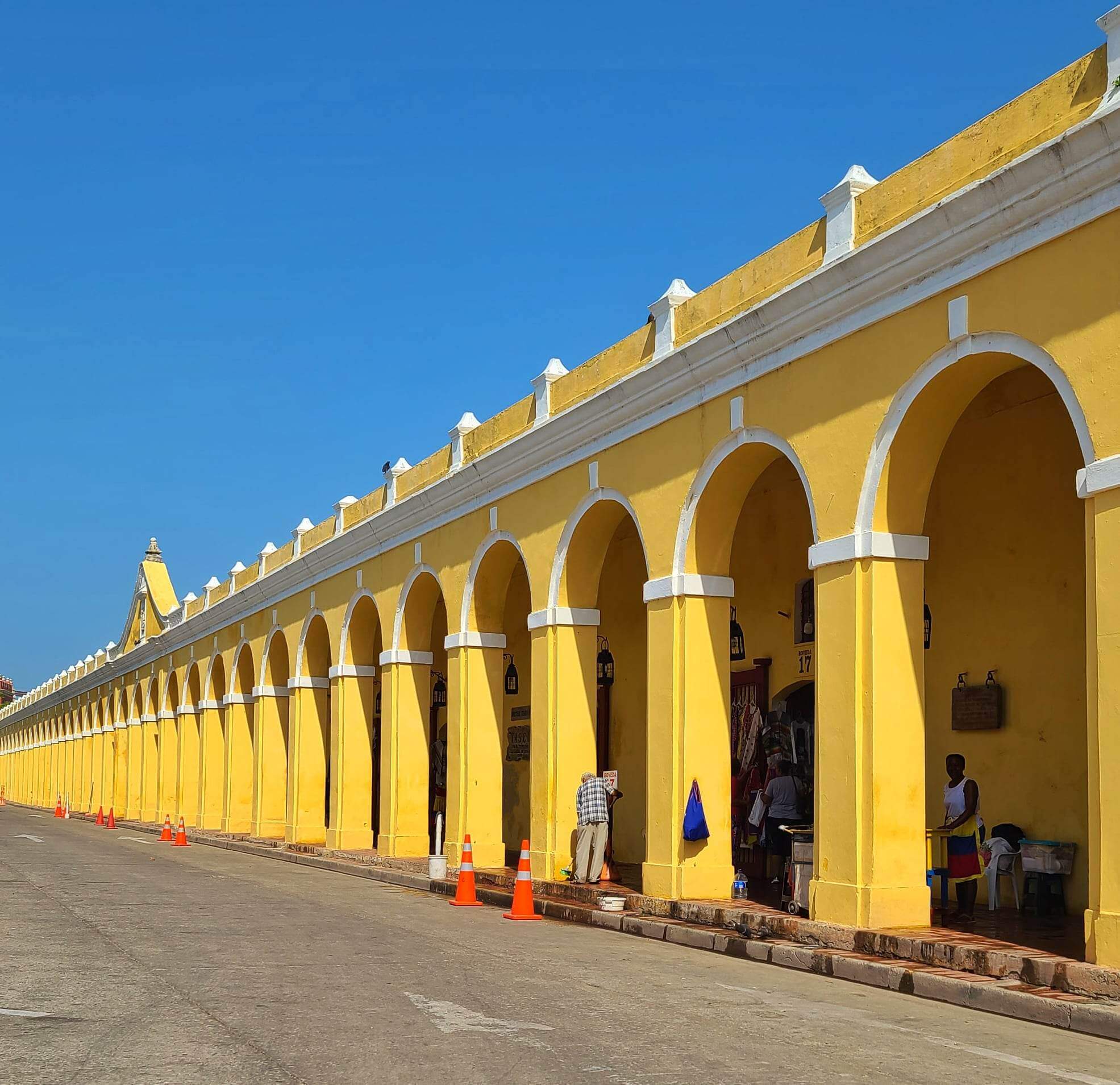 A long row of yellow arched buildings at Las Bovedas market in Cartagena, Colombia, with bright blue sky above.