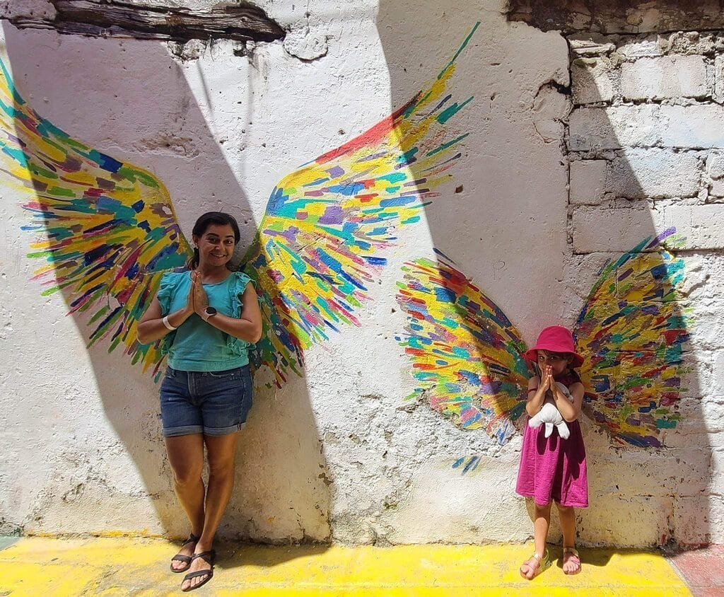 A woman and a child posing in front of colorful painted wings on a wall in Getsemaní, Cartagena, Colombia.