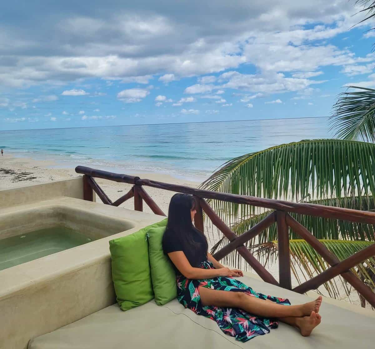 Choosing Between Playa Del Carmen and Tulum Woman lounging on a terrace with a scenic ocean view in Tulum, Mexico.