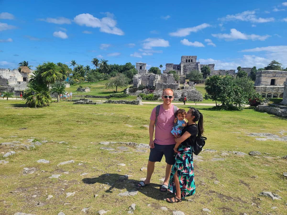 A family posing in front of the ancient stone structures of Tulum ruins in Mexico on a bright, sunny day with clear blue skies.