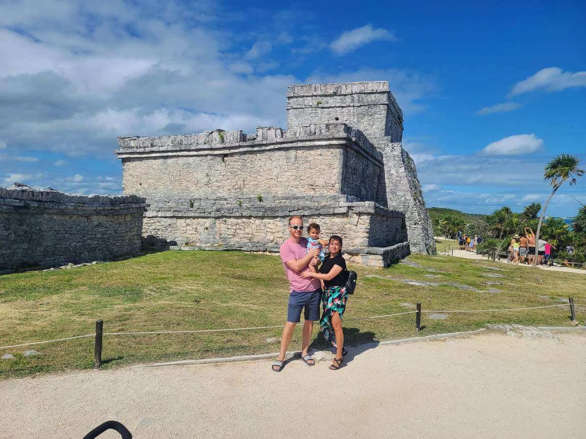 A family posing in front of the historic stone structures at the Tulum Ruins, under a bright blue sky in Tulum, Mexico.