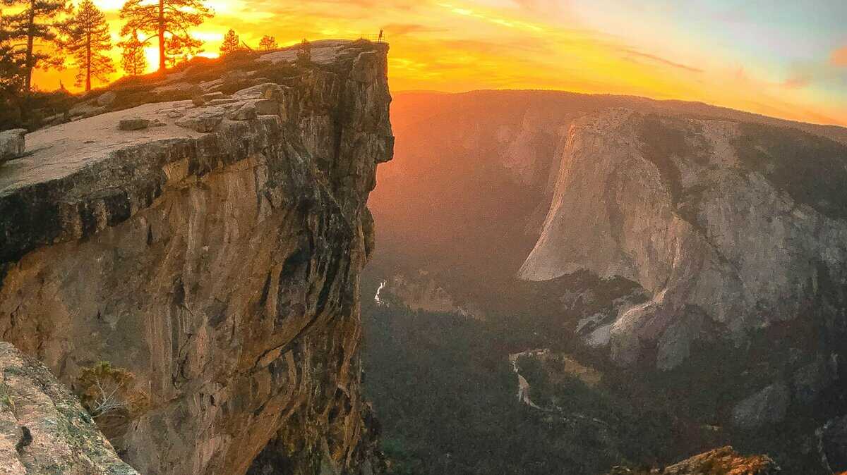 A stunning view from Taft Point in Yosemite National Park, showcasing a dramatic cliff edge with a person standing near the precipice, against the backdrop of a breathtaking sunset.