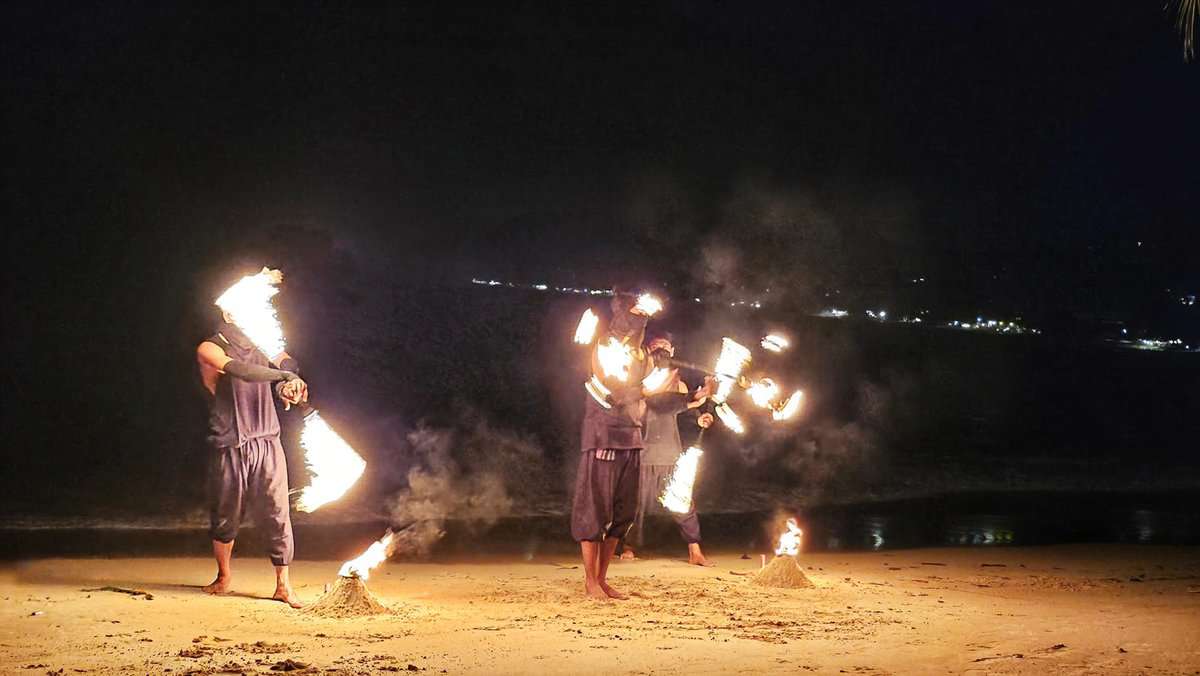 Fire performers on a beach at night in Koh Phi Phi, Thailand, spinning and juggling fiery objects.